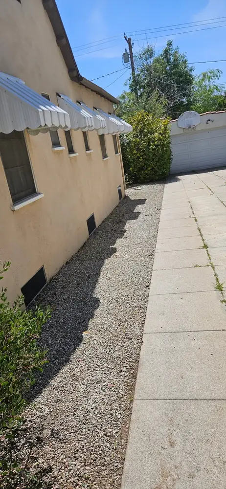 A gravel side yard beside a stucco home and a concrete drive