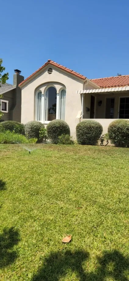 A stucco home with rounded shrubs and a green lawn
